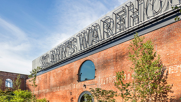 Exterior of St Ann's Warehouse, New York, a redbrick building with its name in neon lights