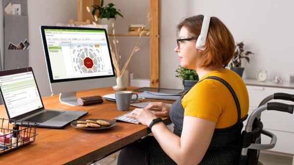 Wheelchair user wearing headset at home office desk with Spektrix seating plan on desktop