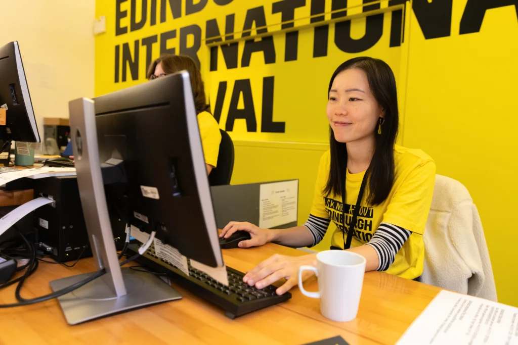 A Theatre Worker Sits In Front Of A Sign For The Edinburgh International Festival