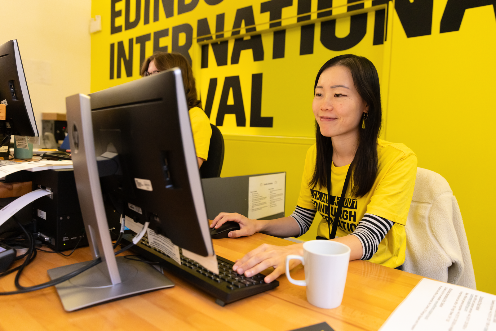 A Theatre Worker Sits In Front Of A Sign For The Edinburgh International Festival