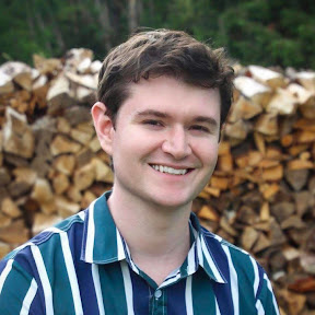 Jake, a white man in his 20s with brown hair, wearing a striped blue, green, and white shirt, smiling at the camera in front of a forested background.