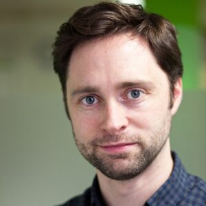 A headshot of Mike Powell, a white man with dark hair in a dark blue shirt.