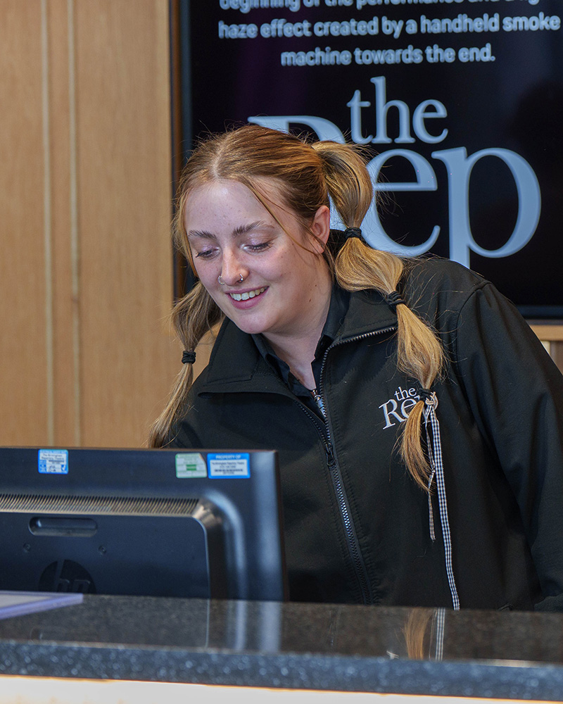 Smiling Theater Worker Sitting At Computer At A Box Office Desk