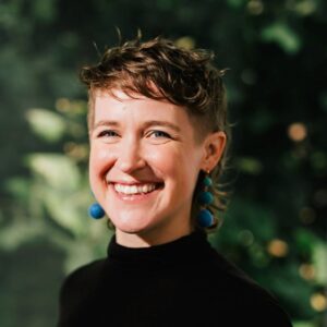 A headshot of Veronica Barron wearing a black mock neck shirt and blue earrings.