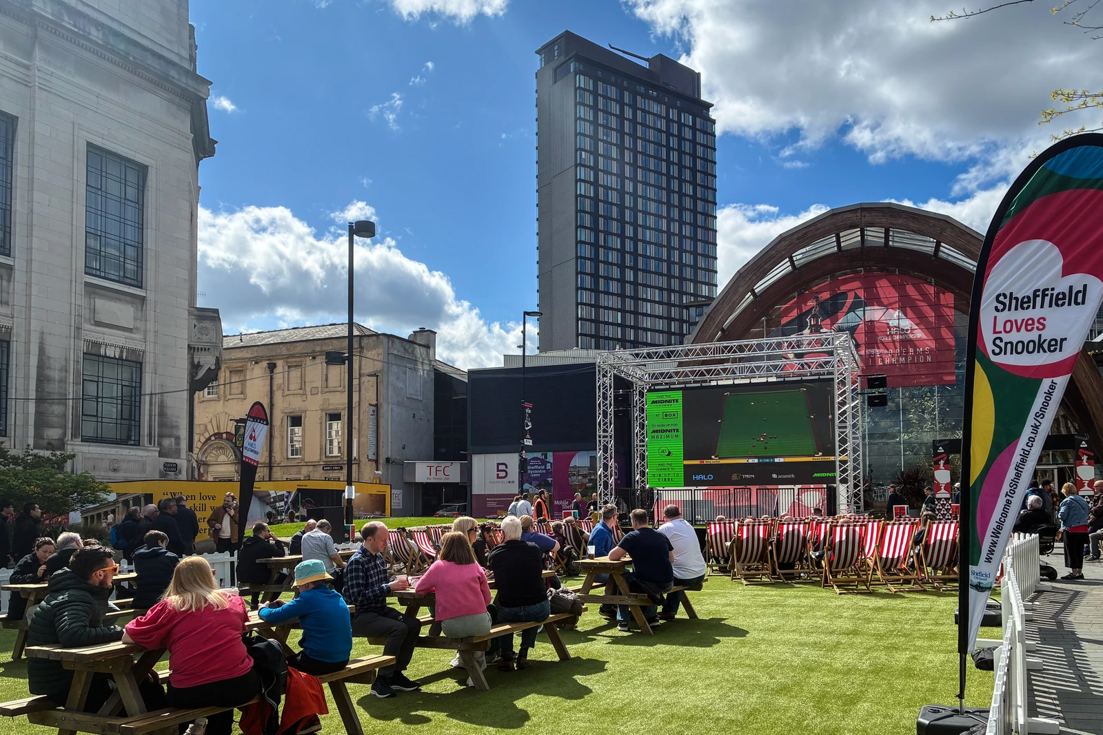 Fans Sit At Picnic Tables Watching Snooker On A Large Outdoor Screen In Tudor Square, Beside A “Sheffield Loves Snooker” Flag.